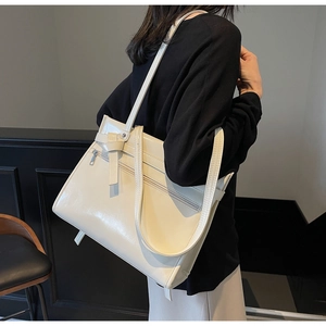 Detail of a creamy beige oversized tote bag in glossy faux leather worn by a model