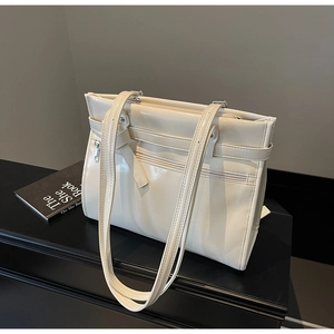 Close-up of cream white patent leather tote bag with stylish zipper and belt details