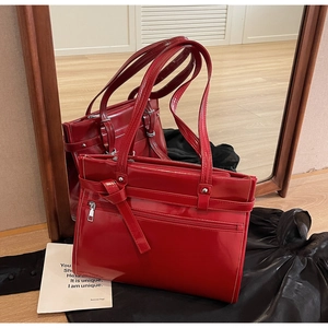 Detail of red glossy patent leather tote bag with unique belt buckle decoration and zipper
