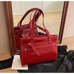 Red glossy handbag with front zipper and strap details reflecting in a mirror