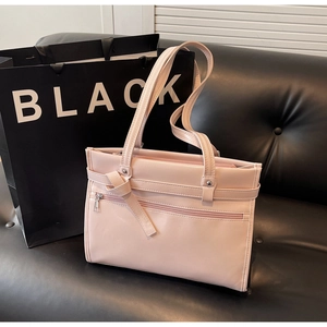 Detailed close-up of glossy pink faux leather handbag with knot decor on black sofa