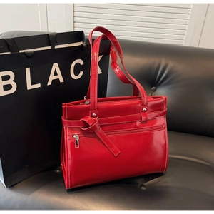 Close-up of red patent leather tote bag with stylish knot detail on a black sofa