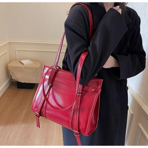 Detail of red glossy leather tote bag with silver buckles and dual straps shown on a model