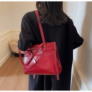 Rear view of a model wearing a shiny red patent leather tote bag with functional zipper pocket
