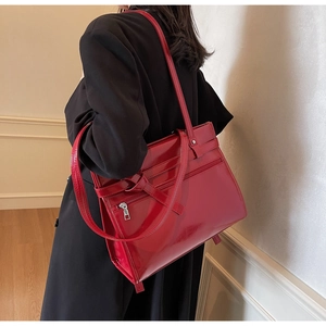 Detail of red patent leather tote bag with stylish buckles worn by model in black suit