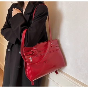 Detail of red glossy tote bag with zipper pocket and knotted strap worn with black suit