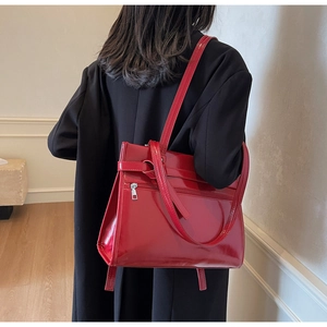 Detail of red patent leather tote bag on black coat showing glossy finish and metal zipper