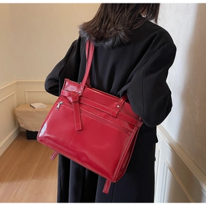 Detail view of a glossy red tote bag with zipper and ribbon on a model wearing black