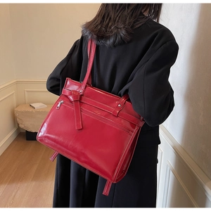 Detail of red glossy shoulder bag with knotted strap and front zipper on model