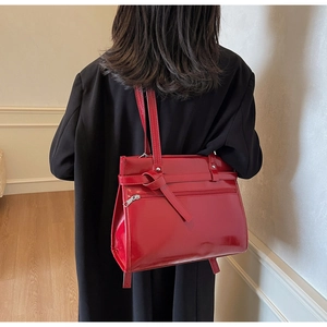 Model wearing a large red patent leather shoulder bag with glossy finish and belt detail