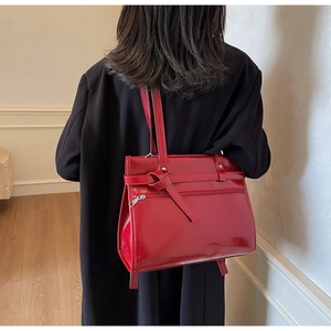 Detail of red glossy leather tote bag with unique knot design on black coat