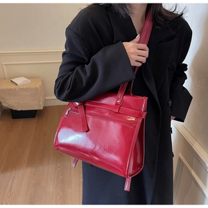 Close-up of vibrant red patent leather shoulder bag worn by model in black blazer