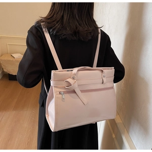 Detail of light pink PU leather bag featuring a zipper pocket and knotted strap decoration