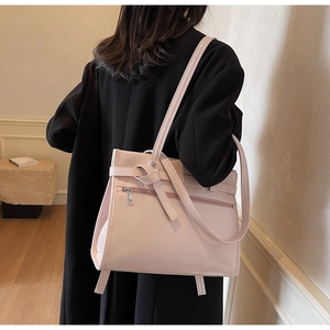 Detail of pink PU leather tote bag with bow accent worn on shoulder over black coat