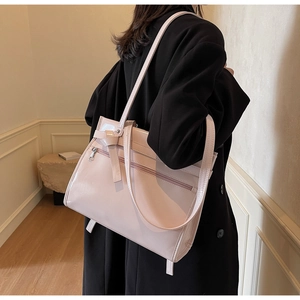 Detail of light pink tote bag featuring a decorative belt, zip pocket, and polished faux leather