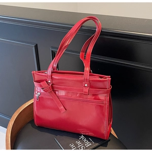 Detail of red glossy patent leather shoulder bag with zipper and decorative knot ties