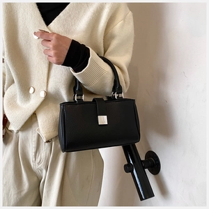 Detail of black pebbled leather handbag featuring a silver square buckle and short handle