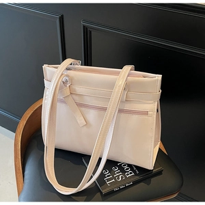 Detail of a pink glossy leather shoulder bag with a decorative strap on a dark chair