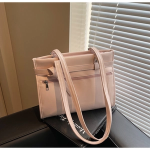 Close-up of pink glossy tote bag with zipper pocket and shoulder straps on a leather bench
