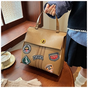 Dettaglio delle toppe vintage e della chiusura dorata sullo zaino marrone su tavolo in legno