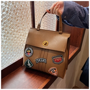 Dettaglio della borsa vintage in similpelle marrone con toppe ricamate e chiusura oro