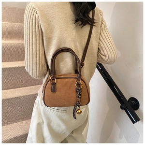 Close-up of brown suede crossbody bag with gold ring hardware and bell charm detail