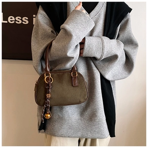 Close-up of matte green suede handbag with brown leather handle and gold bell charm