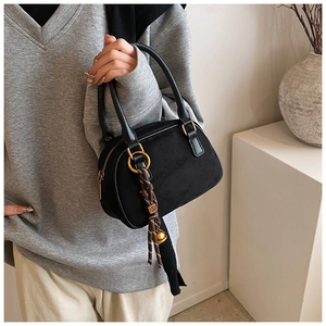 Detail of matte black crescent bag with woven charm and golden bell held by model