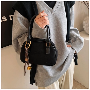 Detail of matte black handbag featuring woven strap and iconic gold charm accessory