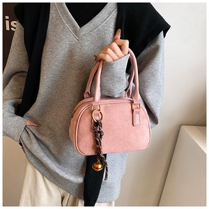 Detail showing the pink suede handbag with woven rope charm and golden bell ornament