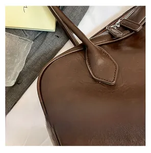 Detail showing silver metal zipper and stitched leather handle of a brown tote bag