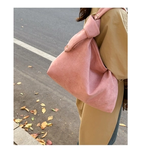 Pink matte suede underarm bag with knot strap detail shown on khaki trench coat