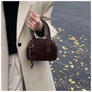 Detail of dark brown suede Boston bag with gold hardware and charm in an autumn setting