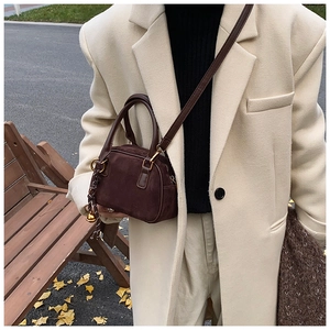 Close-up of matte dark brown suede crossbody bag with gold hardware and spherical charm