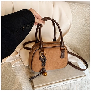 Close-up of brown suede bowling bag with a woven tassel and golden bell charm detail