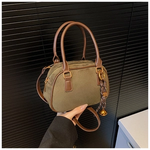 Close-up of olive green suede handbag with brown leather handles and gold zipper detail