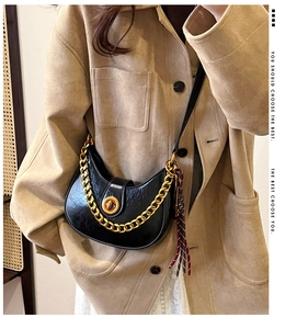 Detail of black crescent shoulder bag featuring gold chain and metallic turn-lock closure