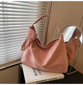 Close-up of matte rose pink suede shoulder bag with unique knotted strap and gold hardware