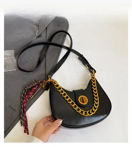 Detail of black crescent crossbody bag with chunky gold chain and woven tassel charm