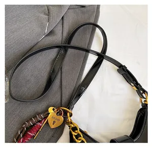 Detail of adjustable strap, gold chain, heart locket and tassel on black crescent bag