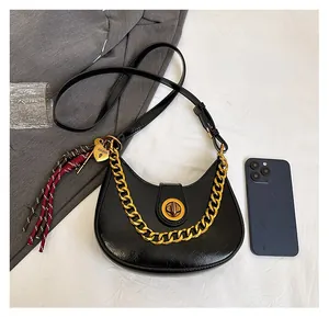 Detail of black leather half-moon saddle bag with gold chain and woven tassel charm