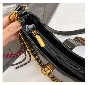 Close-up of smooth gold zipper and decorative chain on a black glossy leather handbag