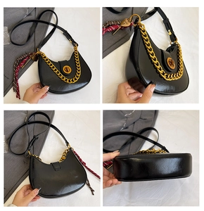 Detail view of black crescent shoulder bag with gold chain and woven silk scarf charm