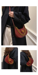 Close-up of wine red saddle bag with gold chunky chain strap and metallic buckle lock