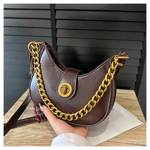 Detailed shot of dark brown crescent bag with glossy texture and gold metal chain