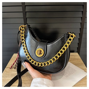 Close-up of black glossy leather moon bag with chunky gold chain and metal clasp