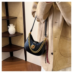 Detail of black oil wax leather hobo bag with thick gold chain and red ribbon accent