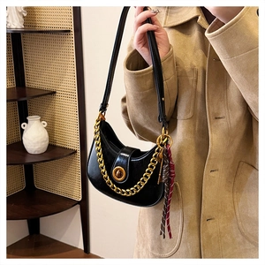 Close-up of black crescent underarm bag featuring a chunky gold chain and tassel detail