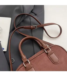 Detail of a brown suede Boston bag with silver hardware on a grey blazer backdrop