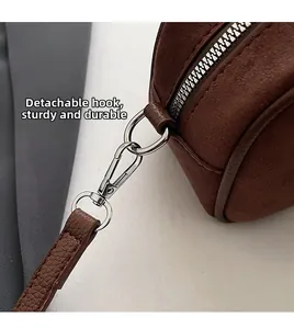 Detail of brown suede handbag featuring silver metal zipper and detachable strap hook